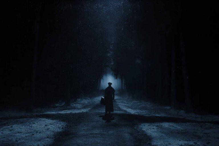 Imagen de Nosferatu en el que se ve un cruce de caminos en un bosque nevado de noche, con niebla y una atmósfera opresiva.